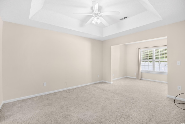 carpeted empty room with a raised ceiling, a ceiling fan, and baseboards