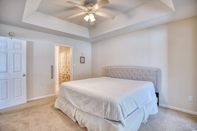 bedroom featuring ceiling fan, light colored carpet, a textured ceiling, and a tray ceiling