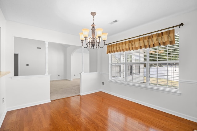 unfurnished dining area featuring arched walkways, a chandelier, wood finished floors, and baseboards