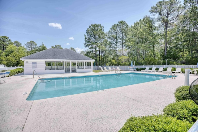 community pool featuring a patio area, fence, and view of scattered trees