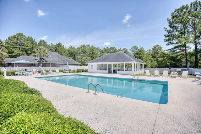 community pool with a patio, fence, and view of scattered trees