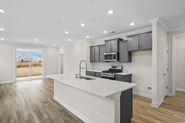 kitchen featuring decorative backsplash, appliances with stainless steel finishes, sink, a center island with sink, and light hardwood / wood-style flooring