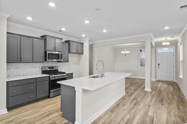 kitchen with light wood-type flooring, ornamental molding, stainless steel appliances, sink, and an island with sink