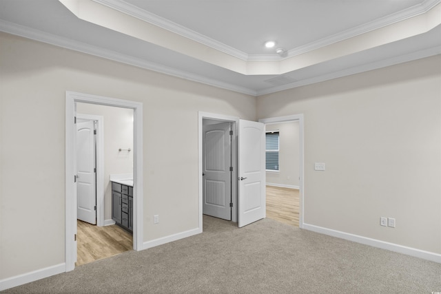 unfurnished bedroom with light carpet, a raised ceiling, ensuite bath, and crown molding