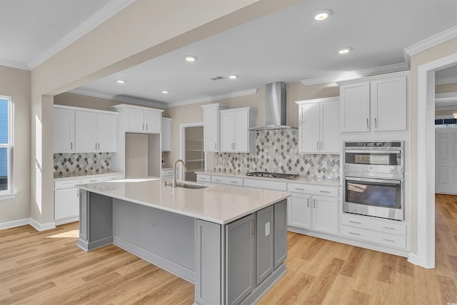 kitchen with white cabinets, wall chimney range hood, sink, and an island with sink