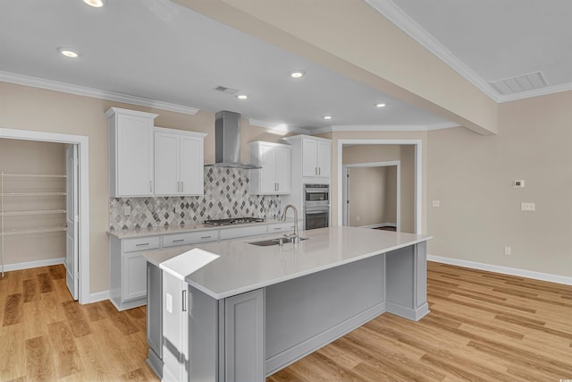 kitchen with white cabinetry, sink, wall chimney range hood, and a center island with sink