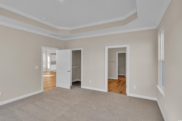 unfurnished bedroom featuring a walk in closet, crown molding, a tray ceiling, light colored carpet, and a closet