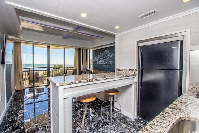 kitchen with black fridge, a kitchen breakfast bar, dark tile flooring, and light stone countertops