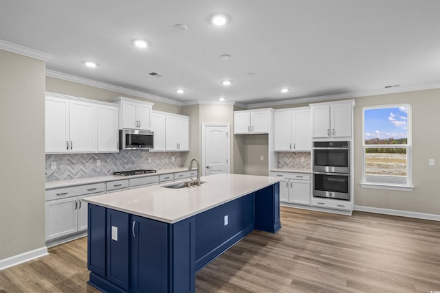 kitchen with a kitchen island with sink, white cabinets, sink, light wood-type flooring, and stainless steel appliances