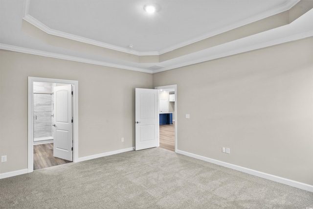 unfurnished bedroom with carpet, ornamental molding, a tray ceiling, and ensuite bath
