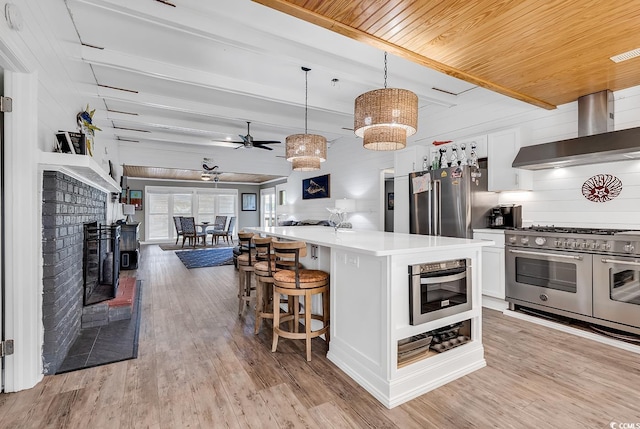 kitchen with decorative light fixtures, high end appliances, light hardwood / wood-style flooring, and wall chimney exhaust hood