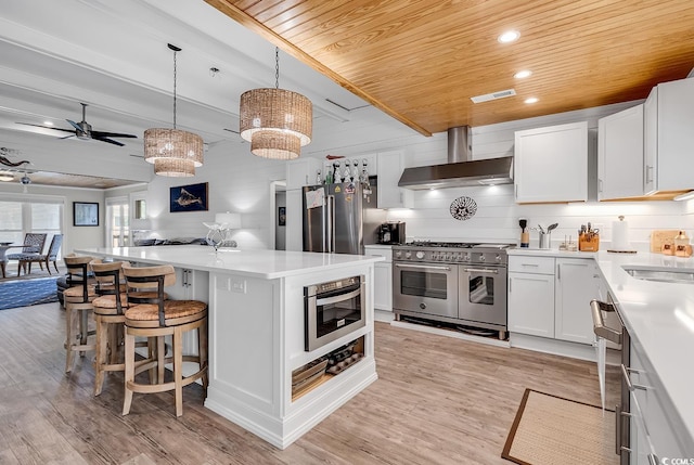 kitchen with light hardwood / wood-style floors, white cabinetry, wall chimney exhaust hood, and premium appliances