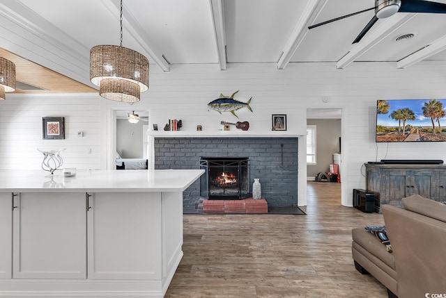 kitchen featuring decorative light fixtures, a fireplace, ceiling fan with notable chandelier, wood walls, and hardwood / wood-style flooring