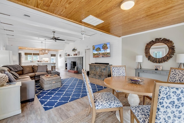 living room featuring a brick fireplace, ceiling fan, ornamental molding, beam ceiling, and wood-type flooring