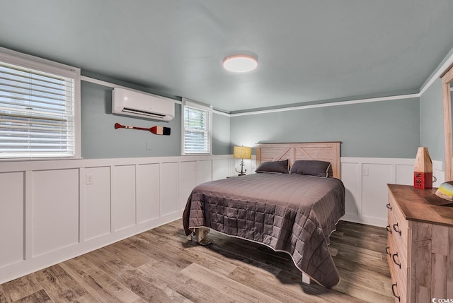 bedroom featuring a wall unit AC, ornamental molding, and light wood-type flooring