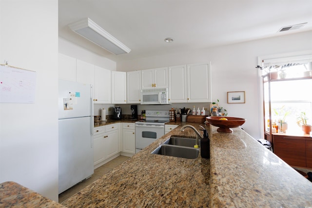 kitchen with white appliances, sink, dark stone countertops, light tile patterned flooring, and white cabinetry