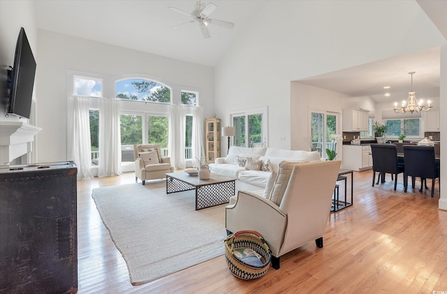 living room with ceiling fan with notable chandelier, light hardwood / wood-style flooring, and high vaulted ceiling