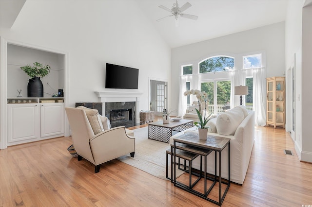 living room featuring a premium fireplace, high vaulted ceiling, ceiling fan, and light wood-type flooring