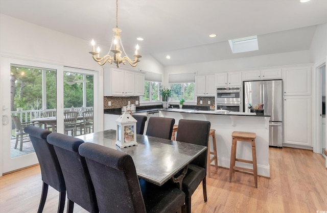 dining space featuring light hardwood / wood-style floors, a notable chandelier, and lofted ceiling with skylight