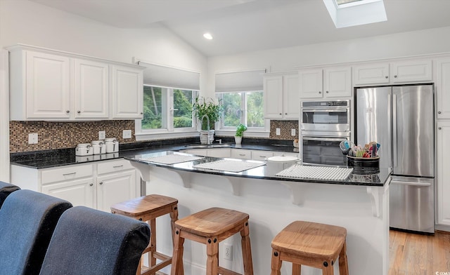 kitchen with decorative backsplash, stainless steel appliances, lofted ceiling with skylight, and light wood-type flooring