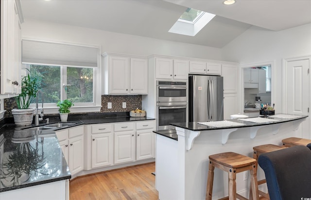 kitchen featuring white cabinetry, vaulted ceiling with skylight, light hardwood / wood-style flooring, and stainless steel appliances