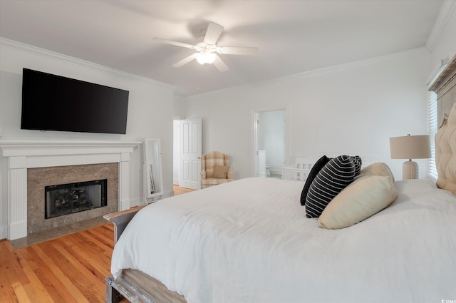 bedroom with crown molding, light hardwood / wood-style flooring, ceiling fan, ensuite bathroom, and a high end fireplace