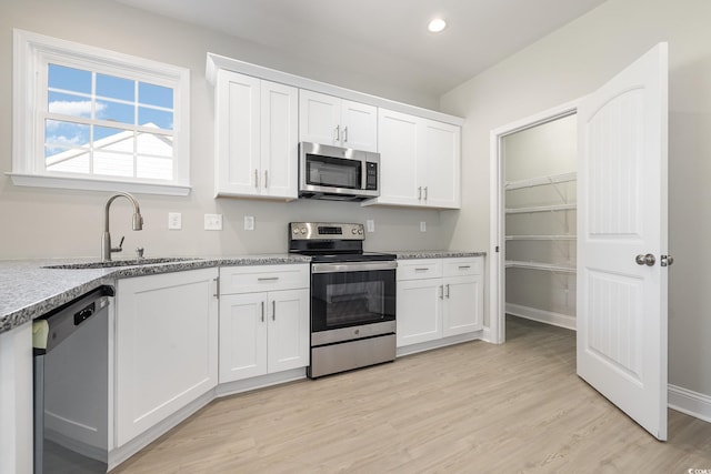 kitchen featuring white cabinets, sink, light stone countertops, light hardwood / wood-style floors, and stainless steel appliances