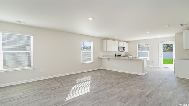 kitchen featuring a kitchen bar, kitchen peninsula, stainless steel appliances, light hardwood / wood-style flooring, and white cabinets