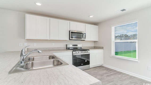 kitchen with visible vents, a sink, stainless steel appliances, light countertops, and white cabinetry