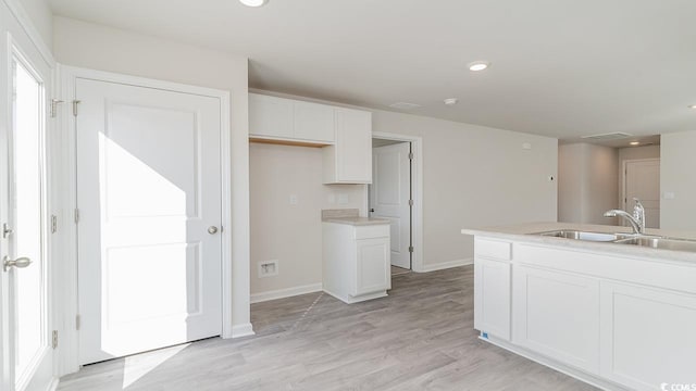 kitchen featuring baseboards, recessed lighting, light wood-style floors, white cabinetry, and a sink