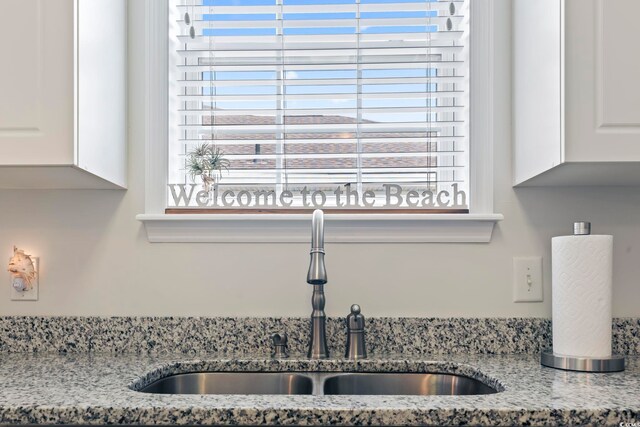 interior details with white cabinets, light stone countertops, and sink