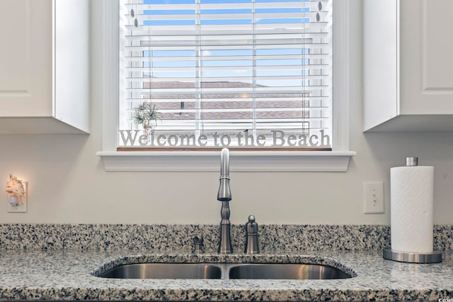 kitchen featuring light stone counters, white cabinetry, plenty of natural light, and sink