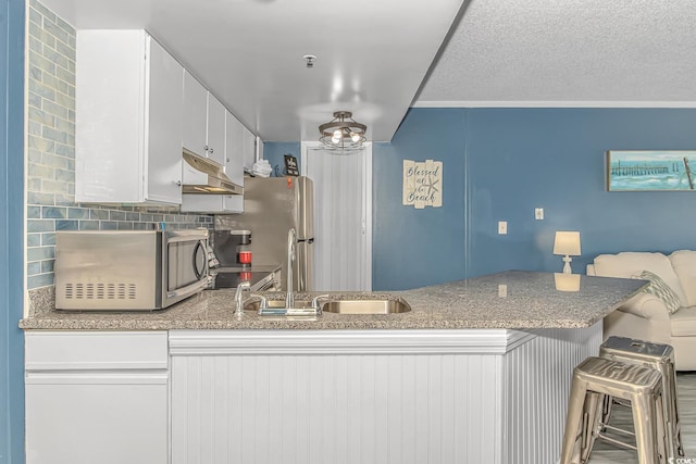 kitchen with a breakfast bar, white cabinetry, appliances with stainless steel finishes, kitchen peninsula, and backsplash