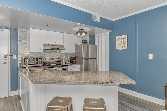 kitchen featuring a breakfast bar, stone counters, appliances with stainless steel finishes, white cabinets, and kitchen peninsula