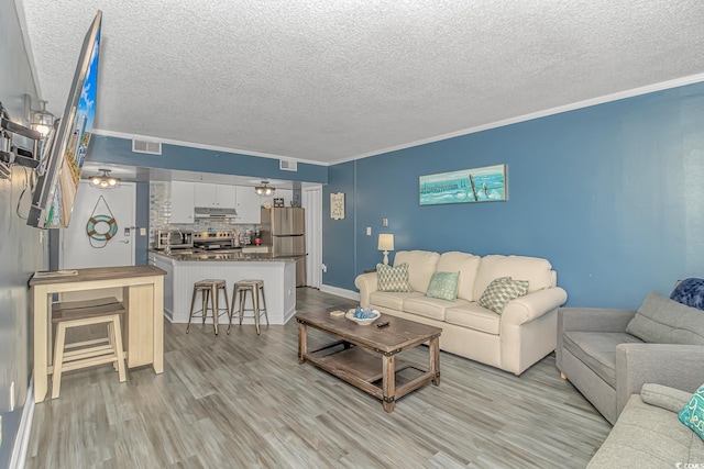 living room featuring crown molding, a textured ceiling, and light wood-type flooring