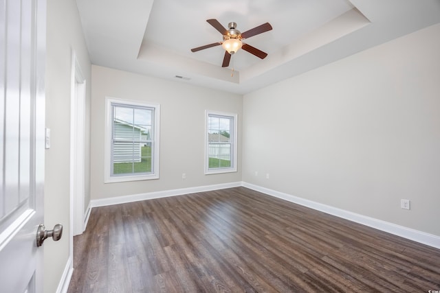 unfurnished room featuring a tray ceiling, ceiling fan, and dark wood-type flooring