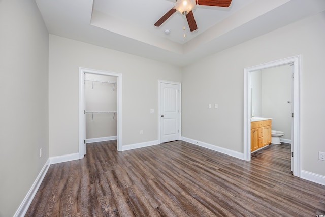 unfurnished bedroom featuring a spacious closet, a raised ceiling, connected bathroom, ceiling fan, and dark hardwood / wood-style floors