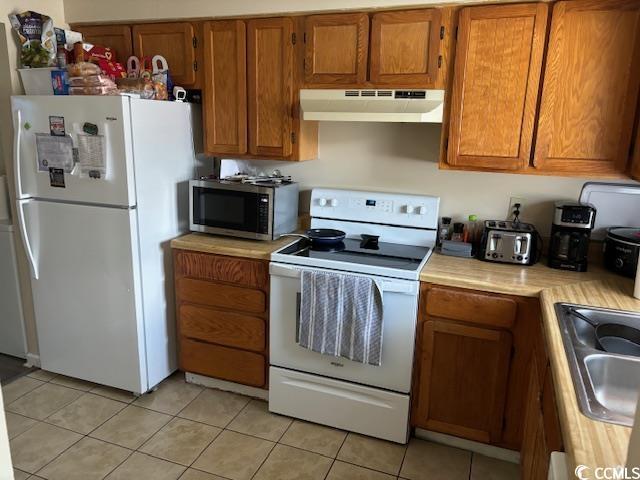 kitchen featuring white appliances, brown cabinets, light countertops, under cabinet range hood, and a sink