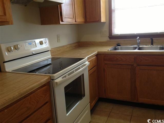 kitchen featuring brown cabinets, white electric stove, light tile patterned floors, light countertops, and a sink