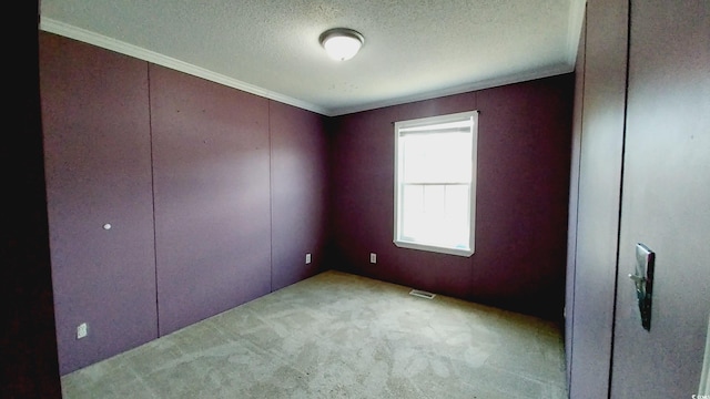 unfurnished room featuring a textured ceiling, ornamental molding, and light colored carpet