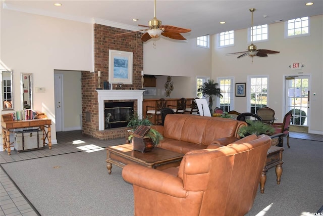 carpeted living room featuring ceiling fan, crown molding, a high ceiling, and a brick fireplace