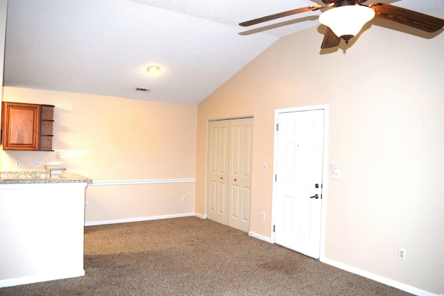 unfurnished room featuring dark colored carpet, a textured ceiling, vaulted ceiling, and ceiling fan