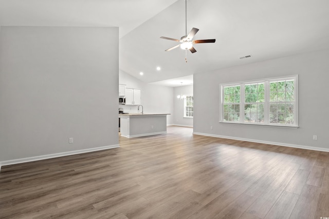 unfurnished living room with high vaulted ceiling, ceiling fan with notable chandelier, hardwood / wood-style flooring, and sink