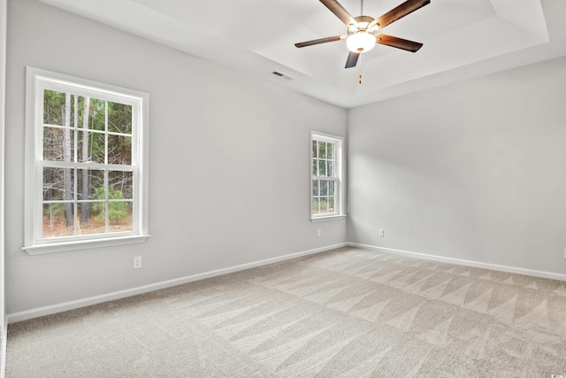 carpeted spare room with ceiling fan, a wealth of natural light, and a tray ceiling