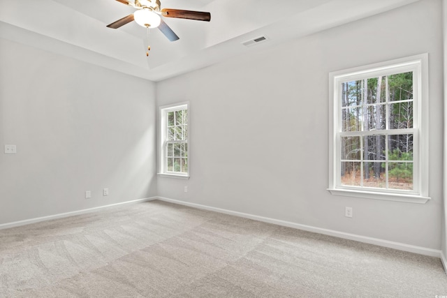 spare room featuring ceiling fan, light colored carpet, and a raised ceiling