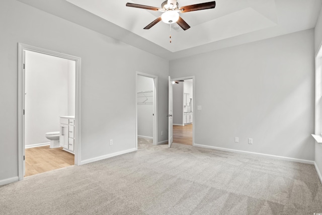 unfurnished bedroom with ceiling fan, connected bathroom, a closet, light colored carpet, and a walk in closet