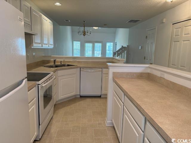 kitchen featuring white appliances, white cabinets, sink, a textured ceiling, and a notable chandelier