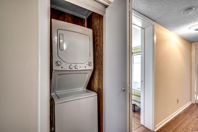 washroom with a textured ceiling, light hardwood / wood-style floors, and stacked washer and clothes dryer