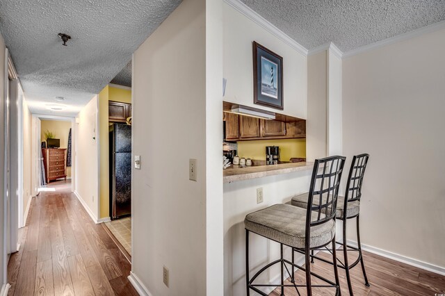 kitchen with black refrigerator, a kitchen bar, wood-type flooring, and crown molding