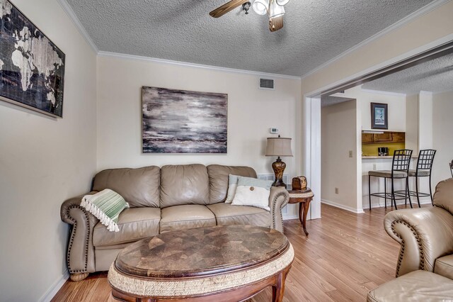 living room with a textured ceiling, ceiling fan, and crown molding